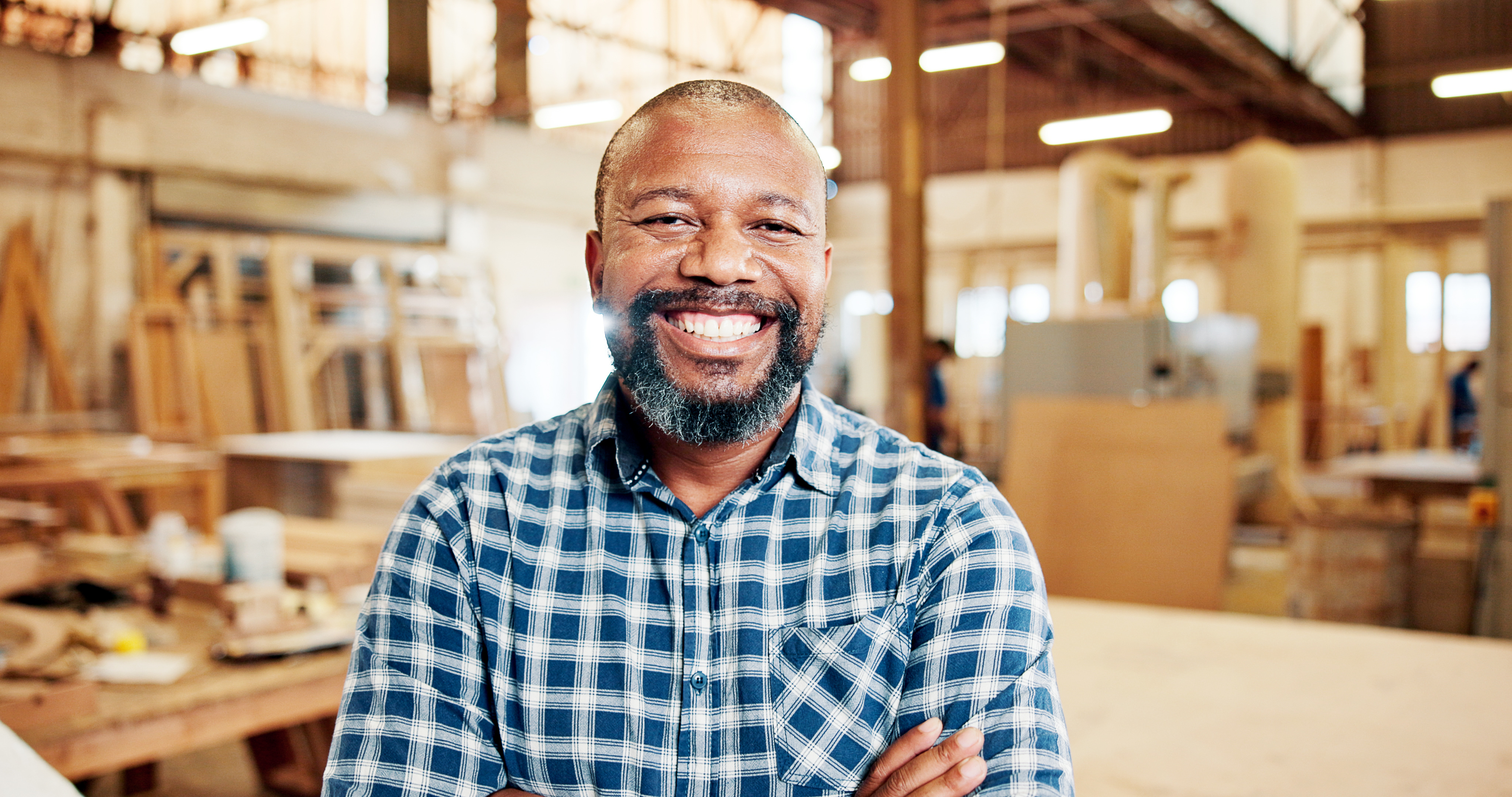 Carpenter, portrait and mature man with arms crossed, workshop and happy for production or creative. Factory, artisan and black person with smile for woodwork, confident and career growth in Nigeria